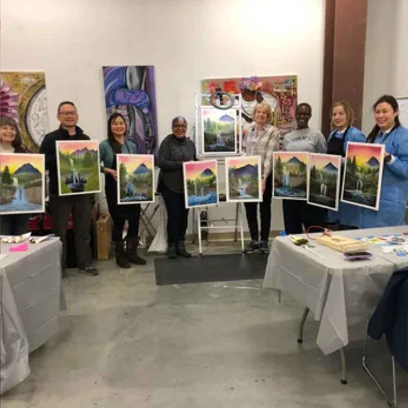 Group displaying landscape paintings in art studio.