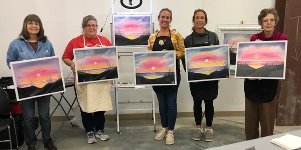 Group displaying sunset paintings in workshop.