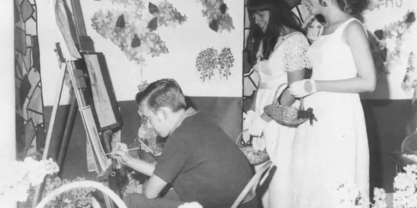 Artist painting while two women observe.