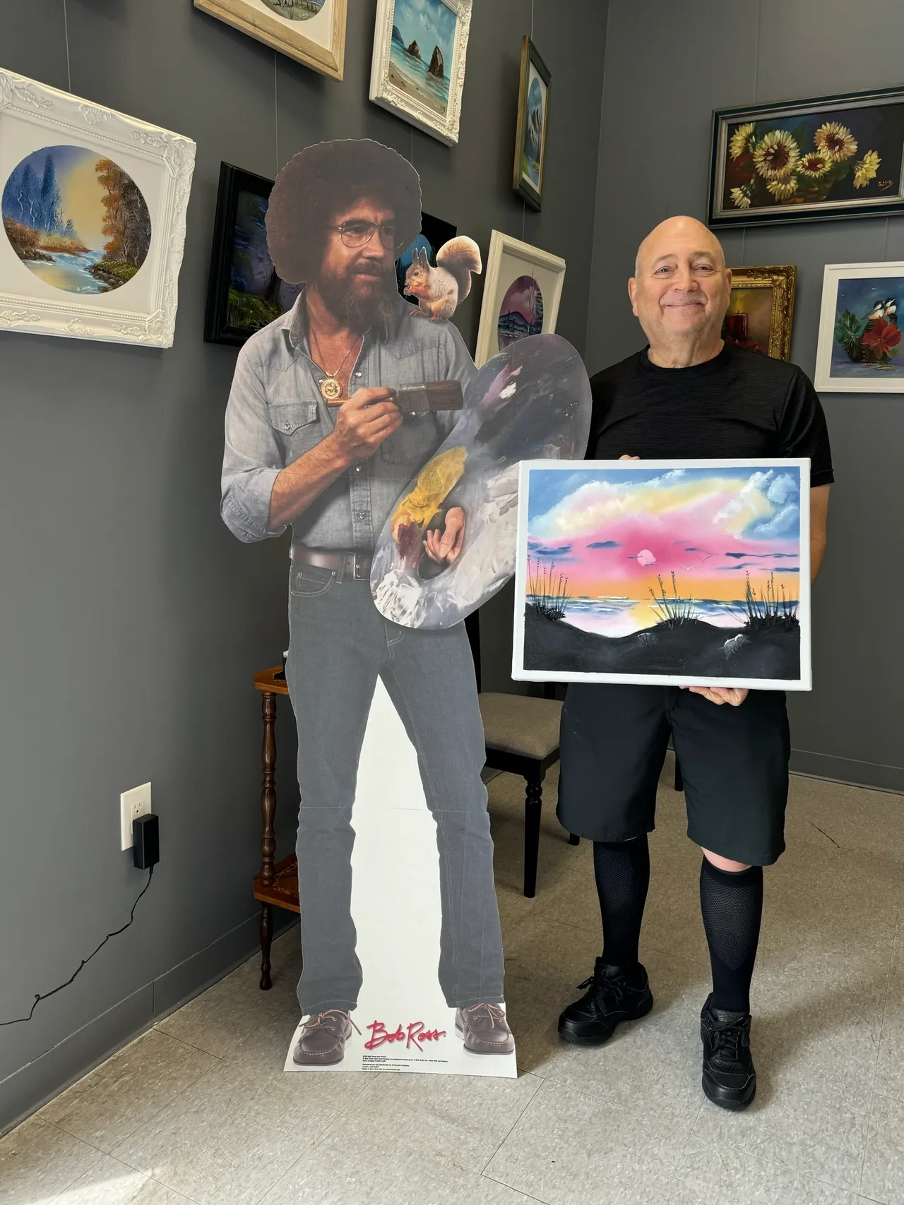 Man holding painting next to artist cutout.