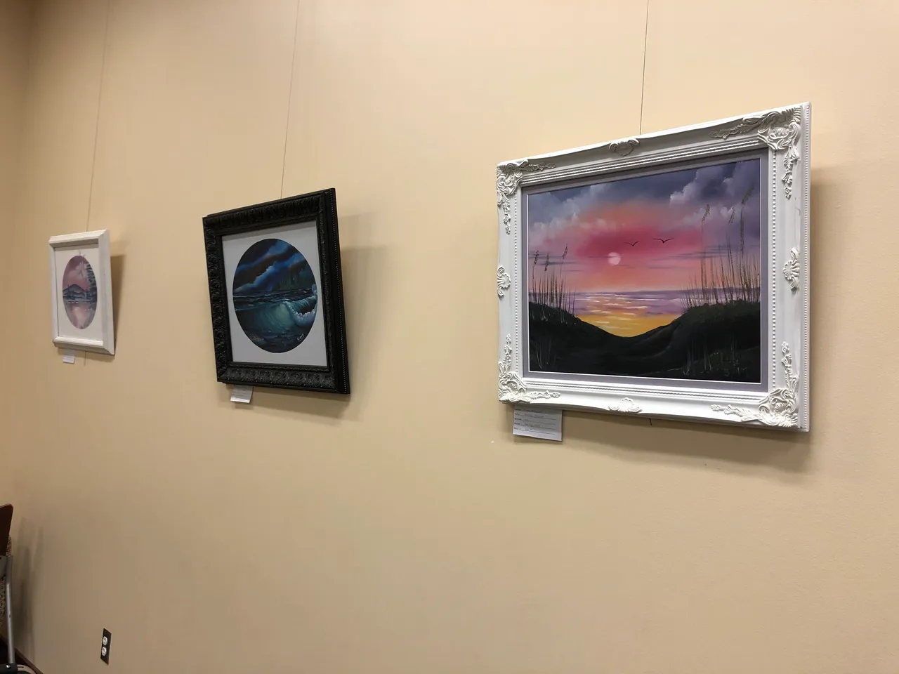 Three framed landscape paintings on display wall.