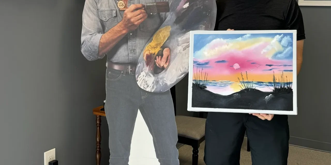 Man holding painting next to artist cutout.