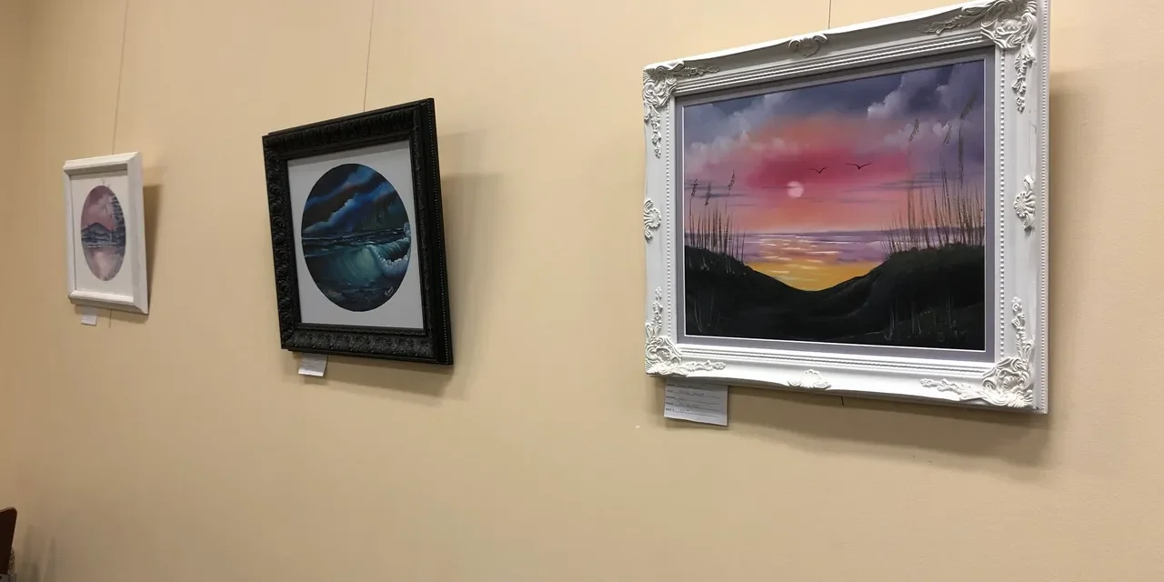 Three framed landscape paintings on display wall.